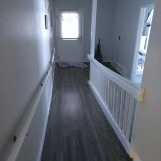 A hallway with handrails, leading to a door and overlooking stairs.