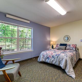 A cozy bedroom with a bed, chair, and large window letting in natural light.