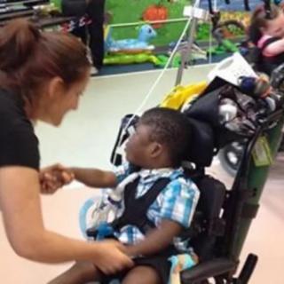A caregiver interacts with a child in a wheelchair indoors.