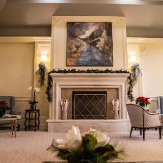 A cozy and elegantly decorated living room featuring a classic fireplace, beautiful artwork, and festive floral arrangements.