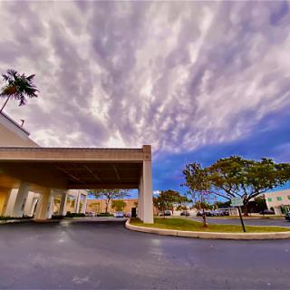 A beautiful view of a building under a dramatic sky with clouds and palm trees.