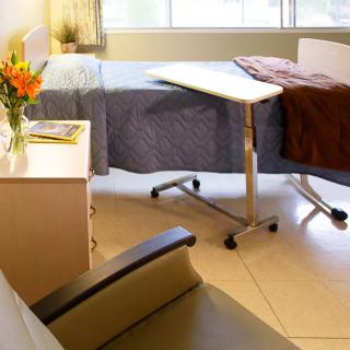 A well-lit hospital room with a bed, side table, and flowers by the window.