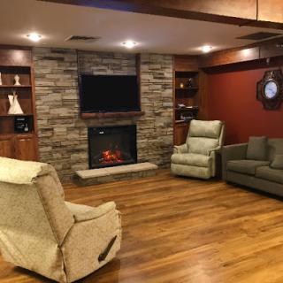 A cozy living room featuring a stone fireplace, comfortable seating, and warm wooden flooring.