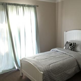 A minimalist bedroom with a single bed and soft curtains allowing natural light in.