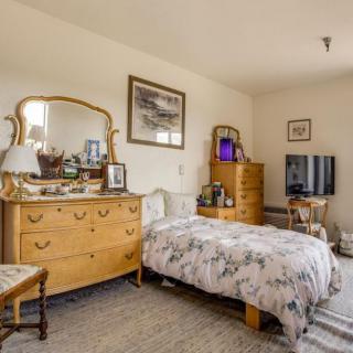 A cozy bedroom with classic wooden furniture, including a dresser with a mirror, a bed, and a television.