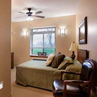 A cozy bedroom with warm lighting, featuring a bed with green bedding, a window view, and elegant furnishings.