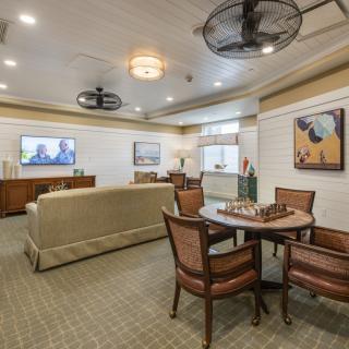 A cozy living room featuring a seating area with a chess board on the table, artwork on the walls, and a television.
