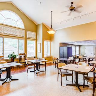 A bright and spacious dining area with multiple tables, chairs, large windows, and a ceiling fan.