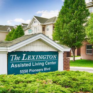 Sign for The Lexington Assisted Living Center in front of a residential building surrounded by greenery.