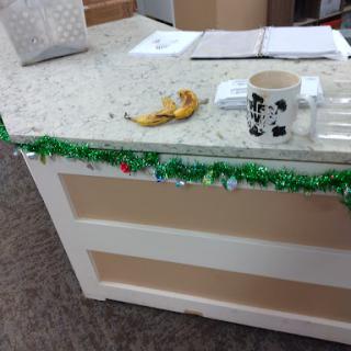An office counter decorated with holiday garland, featuring a banana and a coffee mug.