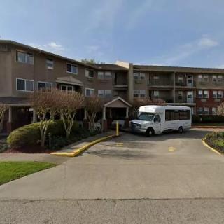 A residential apartment building with a shuttle bus parked in the driveway.