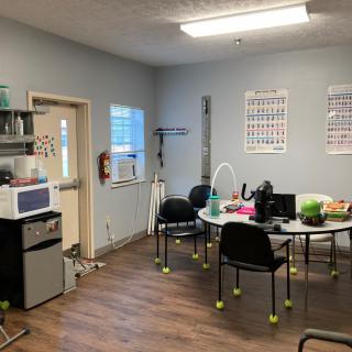A small medical office with a table and chairs, featuring posters on the walls and various equipment.