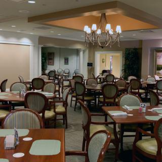An elegant dining area with neatly arranged tables and chairs, illuminated by a chandelier.