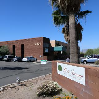 View of a commercial building with a parking lot and palm trees in a desert setting.