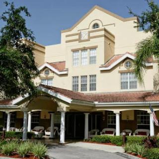 A beautiful residential building with a welcoming front entrance, surrounded by lush landscaping under a clear blue sky.