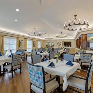 A spacious and elegantly decorated dining area with neatly arranged tables and chairs, illuminated by chandeliers.