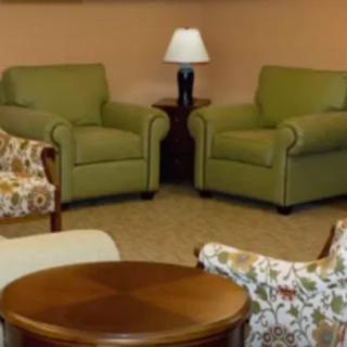 A cozy living room featuring two green armchairs, a wooden table, and a lamp.