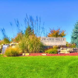 A scenic view of the Prairie Hills neighborhood sign surrounded by lush greenery and vibrant landscaping.
