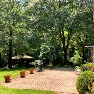 A serene outdoor space featuring a patio surrounded by lush greenery and flower pots, perfect for relaxation and gatherings.