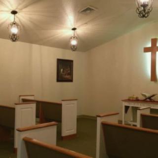 A serene chapel interior with pews, an altar, and a cross on the wall.