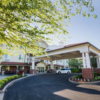 A building entrance with a covered driveway and landscaping under sunny skies.