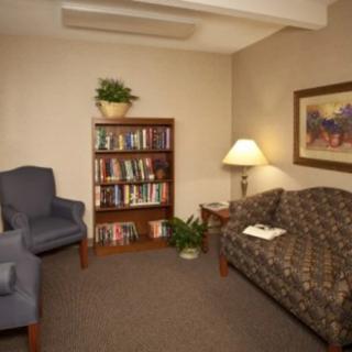 A cozy living room with a couch, armchair, bookshelf, and lamp.