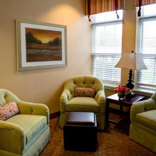A cozy living room corner with three green armchairs, a lamp, and wall art.