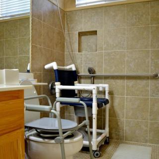 An accessible bathroom equipped with a mobility aid wheelchair, grab bars, and tiled walls.