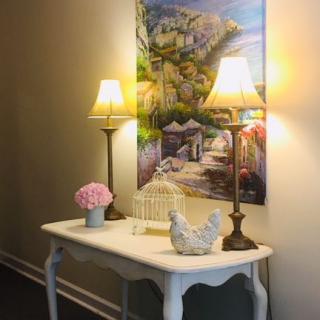 A beautifully decorated table with two lamps, a birdcage, and floral accents beneath a vibrant landscape painting.