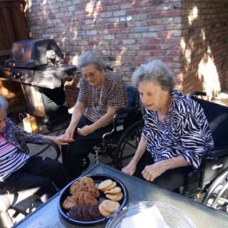 Three elderly women enjoying a sunny day outdoors with snacks.
