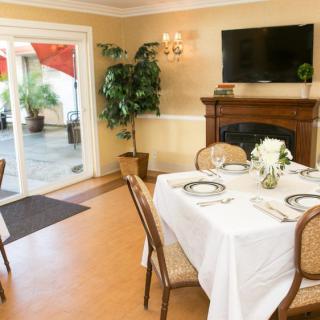 A cozy dining room with a beautifully set table, fireplace, and large windows looking out to a patio.