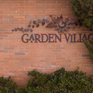 A sign reading 'Garden Village' on a brick wall, surrounded by greenery.
