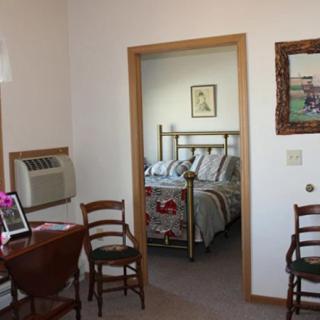 A cozy bedroom with a view of a neatly made bed, a small desk, and chairs in the foreground.