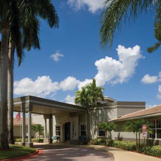 A building entrance surrounded by palm trees under a blue sky with clouds.