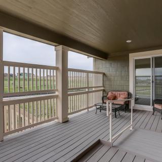 A cozy covered porch with outdoor seating, featuring wooden flooring and railing.
