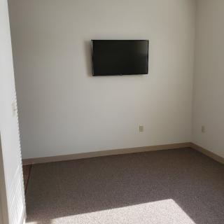 A minimalist empty room with a wall-mounted television and carpeted floor.