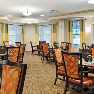 An elegant dining room with multiple tables and chairs, featuring warm d�cor and natural light from large windows.