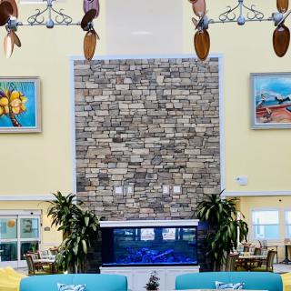 A spacious lobby featuring a large stone fireplace, an aquarium, tropical plants, and decorative artwork on the walls.