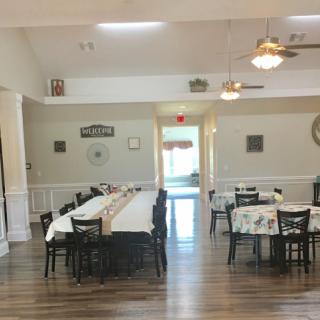 A spacious dining area with neatly arranged tables and chairs, featuring wooden flooring and ceiling fans.