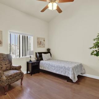 A cozy bedroom with a single bed, armchair, nightstand, and ceiling fan.