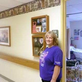 A woman stands in a hallway next to framed decorations, smiling for the camera.