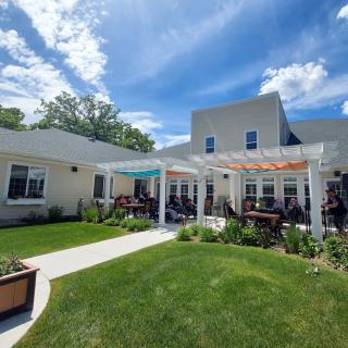 A sunny outdoor patio with a pergola, surrounded by a well-maintained garden.
