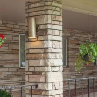 A cozy porch featuring a stone column with a light fixture and hanging plants against a brick wall backdrop.