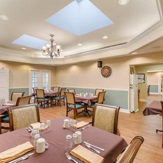 A well-lit dining room with neatly arranged tables and chairs, featuring a chandelier and skylights.