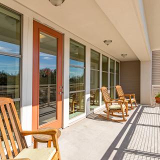 A sunny porch with wooden rocking chairs and large glass doors.