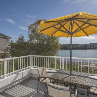 A serene patio with a yellow umbrella overlooking a lake.