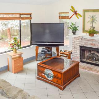 A cozy living room featuring a large television, a wooden coffee table, and a fireplace surrounded by decorative elements.