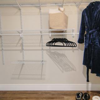 An organized closet with empty shelves, hangers, and a robe hanging neatly.