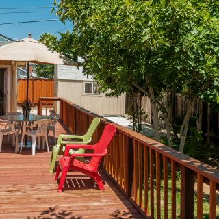A sunny backyard with a wooden deck featuring colorful chairs and an umbrella.