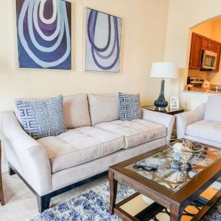 A cozy living room with modern decor, featuring a beige sofa, abstract artwork, and a glass-topped coffee table.